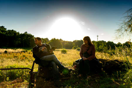 man and woman sitting on a stone wall looking at something that draws attention with the sun almost settingの写真素材