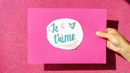 handwritten sign on white paper pasted on a pink cardboard held by one hand with the words je t...