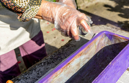 hands with transparent gloves using a purple paint spray to color a rectangular pot