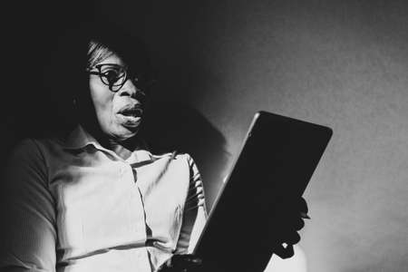 African-American woman talks on old phone sitting on a sofa with satisfied expression in black and whiteの写真素材