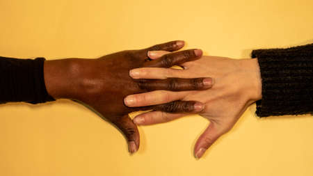 hands with fingers stretched and linked one of them is dark skinned and the other paleの写真素材