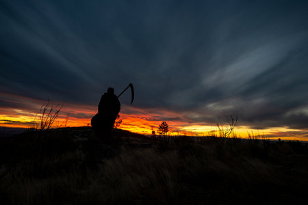 human figure with a scythe on a mountain when the sun sets with a hellish colorの写真素材