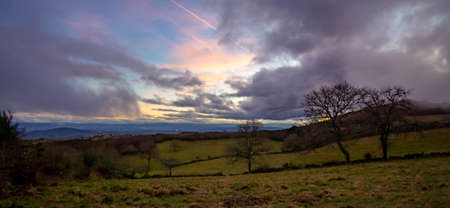 the sun sets somewhere in Galicia where you can see an old building next to a tree and green meadowsの写真素材
