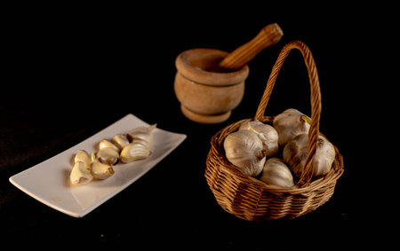 A basket full of garlic heads and next to it a wooden pestle and a tray with peeled clovesの写真素材