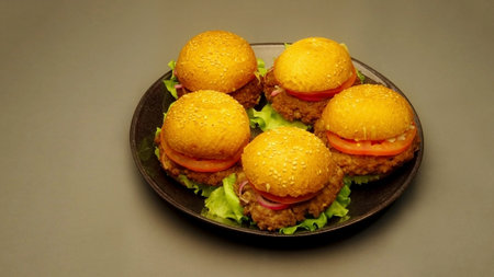 Five homemade hamburgers on black plate on uniform smooth grey backgroundの写真素材