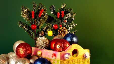 Happy New Year and Chritsmas. Silver, red and blue balls and cones in wooden basket with green christmas tree branches. Homemade christmas toys and decorations on green blured background.の写真素材