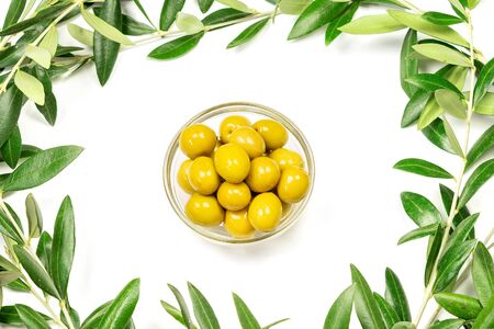 Some olives in a glass bowl and branches of olive tree on the white background.の写真素材
