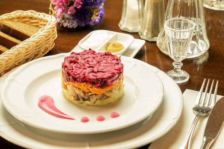 Traditional festive salad of herring and vegetables on the white plate on the table of restaurant. top view, closeup.の写真素材