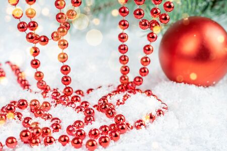 Christmas red bauble and hanging shining decorative beads on the snow white background with blurred lights. Greeting for Christmas.の写真素材