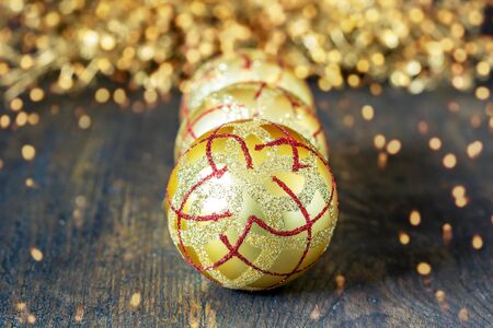 Golden Christmas balls and shining glittering baubles on the wooden natural background closeup. Cristmas art design with bokeh and lights.の写真素材