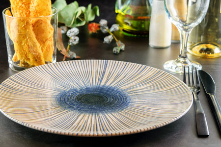 New modern dish with black cutlery, wineglass, cheese chips and some other things on the dark table...