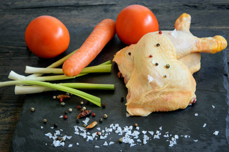 Chicken legs, uncooked, with some vegetables, tomatoes, carrot, green fresh garlic and spices on the...