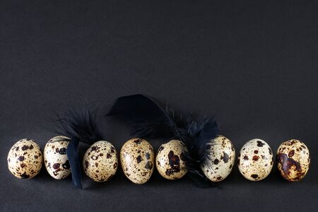 Quail eggs with black feathers on the black background. Dark mode, black minimalistic texture, art decor.の写真素材
