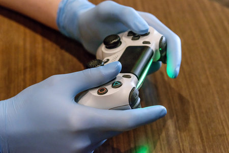 Hands in individual medical gloves handing remote of play station over the the table. Stay safe...