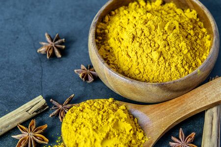 Turmeric powderin wooden spoon and in wooden bowl, cinnamon and anise closeup. Healing spices, health care concept. の写真素材