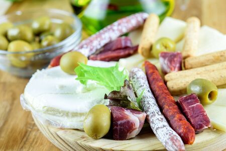 Olives in a glass bowl. Fuet sausages, chorizo sausages, cheese and bread sticks on the wooden plate. Tasty mediterranean fast food. の写真素材