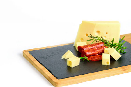 Emmental cheese with rosemary and chorizo sausage on the black cutting board, white background....