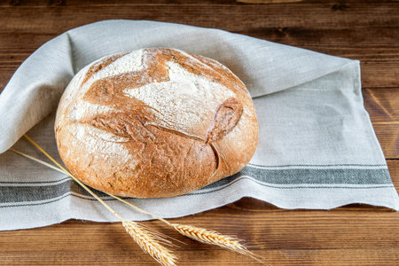 Loaf of integral bread on the kitchen napkin closeup. Spikelets of wheat on the wooden kitchen...