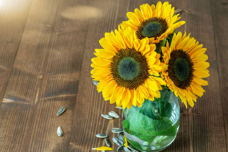 Nice sunflower bouquet in the glass vase on the wooden background closup, top view.の写真素材
