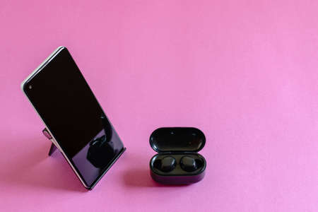 Wireless earphones, mobile phone on the phone stand, pink background. Modern technologies concept.の写真素材