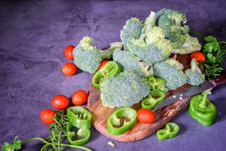 Fresh organic broccoli, tomatoes cherry, pepper and herbs on the cutting board, on the dark background, prepared for cooking. Healthy vegetarian food, healthy life style.の写真素材