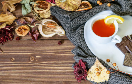 A cup of tea with lemon on the warm winter pullover, dry colorful leaves and flowers, petals on the...