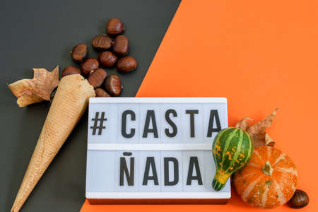 Waffle ice cream cone with chestnuts, decorative pumpkins and party invitation on the black-orange background.の写真素材