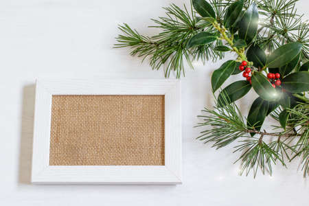 White wooden picture frame with burlap fabric blank, green plant branches on white background. Nice design for greeting card or party invitation for Christmas and any other holiday.の写真素材