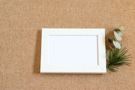 Wooden picture frame with white blank on the eco friendly burlap textured clothes. Mock up photo, top view. Base design for any card greeting or any purposes.の写真素材