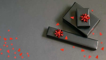 Handmade Christmas gift boxes wrapped in black paper, red sparkle ribbons and festive confetti. Care package, handmade gifts, diy concepts.の写真素材