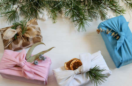 Christmas handmade gift boxes wrapped in reuse cloth in japanese furoshiki style. Festive white background with christmas tree branches, copy space. Care package, diy concepts.の写真素材