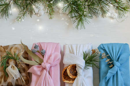 Christmas handmade gift boxes wrapped in reuse cloth in japanese furoshiki style. Festive white background with christmas tree branches,bokeh lights, copy space. Care package, diy concepts.の写真素材