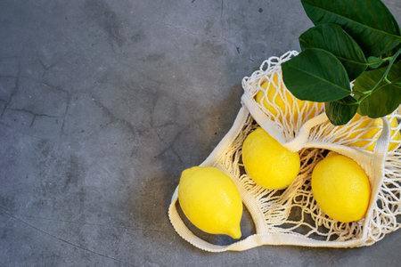 Ripe fresh lemons in white string shopping bag on the gray background. Eco friendly food, no plastic. Healthy clean eating concepts.の写真素材