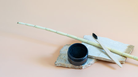 Activated organic charcoal powder in a box and bamboo toothbrush on natural stones and neutral beige background for teeth whitening. Teeth care, wellness concepts.の写真素材