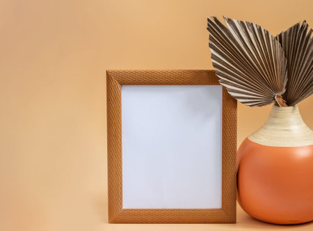 Round vase with dry leaves of sugar palm and wooden picture frame on the beige neutral background....