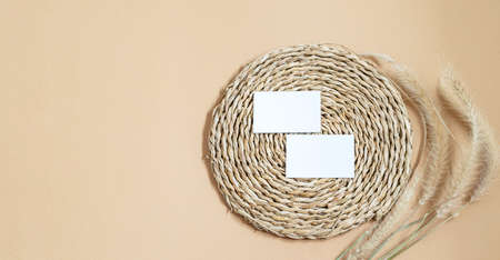 Business cards white blank on the woven straw napkin, natural wheat spikelets on the beige neutral background. Flat lay, mockup  banner for displaying your logo or brand or any more purposes.の写真素材