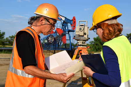 Two land surveyor engineers at work on an European oil well. Petroleum pumpjack  in backgroundの写真素材