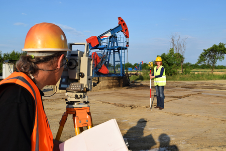 Two land surveyor engineers at work on an European oil well. Petroleum pumpjack  in backgroundの写真素材