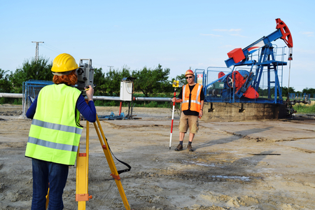 Two land surveyor engineers at work on an European oil well. Petroleum pumpjack  in backgroundの写真素材