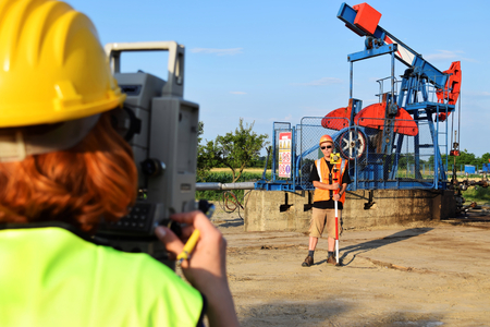 Two land surveyor engineers at work on an European oil well. Petroleum pumpjack  in backgroundの写真素材