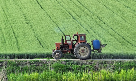 Old red tractor working in farmland during springの写真素材