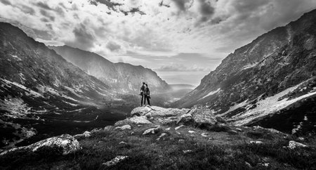 Wide landscape shot with mountains, valley and forest in background. Young couple standing on a...