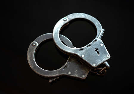 Police metal handcuffs on black isolate. Arrest of the suspect. Criminal news. Restriction of freedom.の写真素材