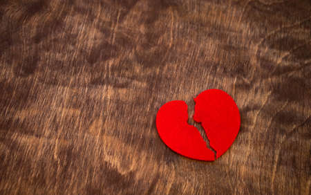 A red heart, broken in half, lies on a wooden table.Broken love. A rag heart made of felt fabric.の写真素材