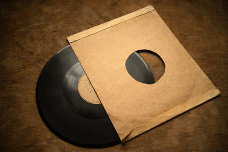 An old vinyl record with a white envelope is lying on a wooden table. Photo in vintage style.の写真素材