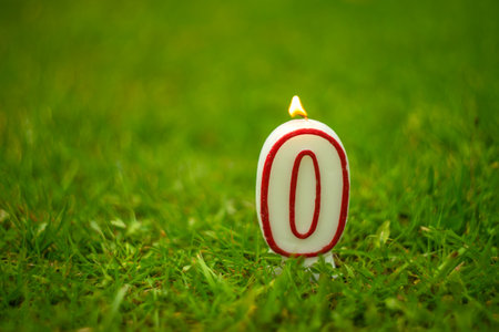 A burning candle with the number zero on the green grass.の写真素材