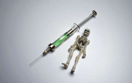 A skeleton next to a syringe on a white isolate. Death by injection. A dangerous vaccine.A glass syringe with poison.の写真素材