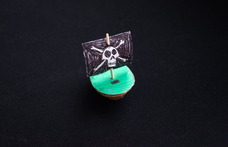 A pirate ship made of walnut shells on a black background. A black pirate flag with a skull. A toy...