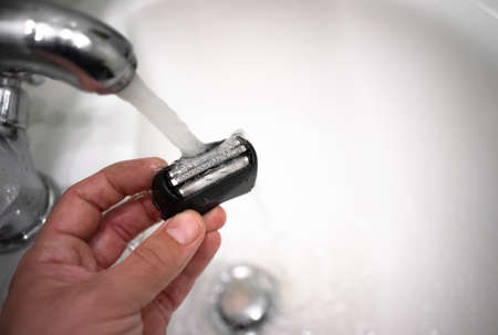 Cleaning the blades of an electric shaver under a stream of water in the faucet. a hand with a razor blade.の写真素材
