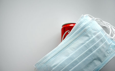 A red soda can is covered with medical masks. Lemonade in a pandemic.